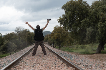 Hombre con los brazos en alto llevando una cámara por medio de la vía de tren