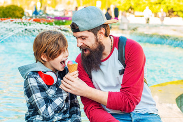 Son teenager and dad eat ice cream in the town square. Fool around biting together one ice cream. Family values. Male friendship
