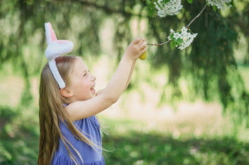 Cute funny girl with Easter eggs and bunny ears at garden. easter concept. Laughing child at Easter egg hunt.