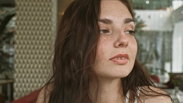 Smiling russian woman looking out while sitting in a quiet metropolitan cafe with soft natural lighting. Medium close up shot on 4k handheld