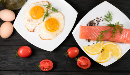 red fish, fried eggs with vegetables on a black wooden background