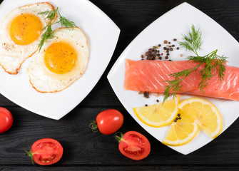 red fish, fried eggs with vegetables on a black wooden background