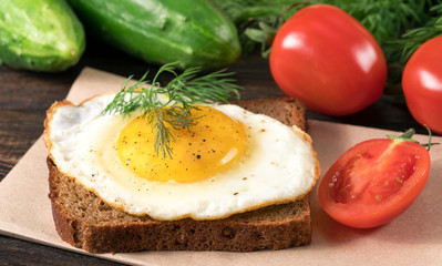 .sandwich with fried egg tomatoes and cucumbers on wooden background