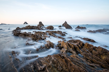 Long exposure fluffy ocean mists rush over tidal pool rocks at the beach