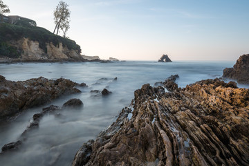 Long exposure fluffy ocean mists rush over tidal pool rocks at the beach