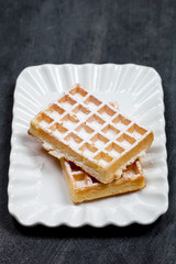 Belgium waffers with sugar powder on ceramic plateon black board background.