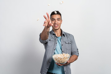 man holding a plate of popcorn in his hands and throwing popcorn at the camera