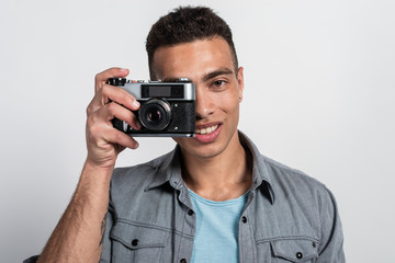 Fototapeta premium Smiling man holding a retro photocamera against his face and looking at the camera- Image