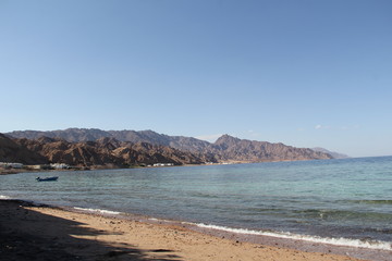 sandy seashore with a boat in the bay and mountains on the horizon