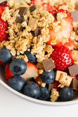 Healthy muesli or cereal breakfast bowl with granola made of rolled whole grain oats, organic honey, milk chocolate chips and tiny graham cracker cookies served with fresh strawberries and blueberries