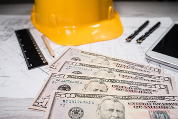 Construction industry costs money us dollars banknotes by tools safety equipment and blueprints