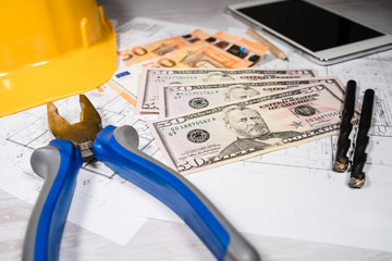 Construction industry costs money banknotes us dollar euro by tools safety equipment and blueprints