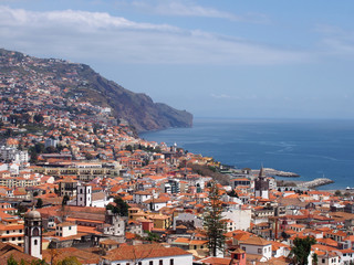 a sunlit view of the city of funchal from above with rooftops and buildings in front of a bright...