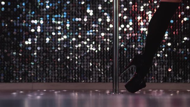 Young stripper in black dances sexually with pylone in night men's club. Poledance. Close-up legs of unrecognizable woman doing tricks with pole.
