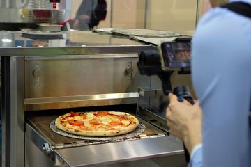Ready Italian pizza on thin dough, fresh from the oven, production equipment. orerator shoots video production. 