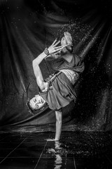 cool and happy korean young guy break dancer in style of bboying doing complex tricks on floor with water splashes and liquid drops effects in aqua zone photo studio with black isolated background