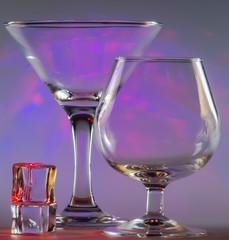Martini Glass together with Cognac Glass and ice cubes with flashing smooth violet lights on background