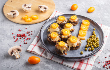 stuffed fried champignons with cheese, kumquats and green peas on a gray concrete background. side view, close up.