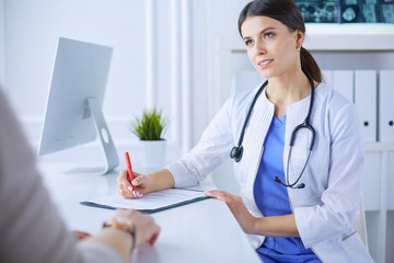 Doctor and patient discussing medical problems in a hospital consulting room. Doc filling in a patient's form