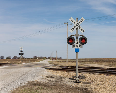 railroad crossing with warning sign and lights in countryside with a gravel road