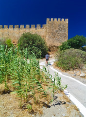 Fragocastelo castle in Crete island, Greece. Bright summer day, clear blue sky. One man walking on cement path towards the castle.