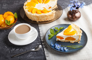 A piece of peach cheesecake on a blue ceramic plate with blue flowers and a cup of coffee on a black concrete background. side view,
