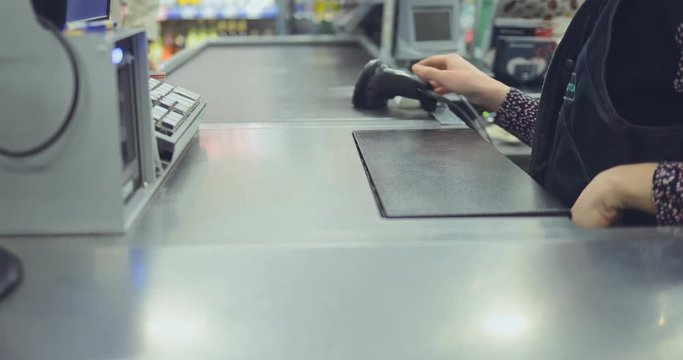 Store employee sits at the checkout counter and punches groceries. Buyer lays out products.