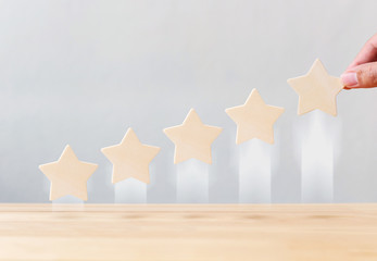 Hand holding wooden five star shape growing growth increase quality on table. The best excellent...