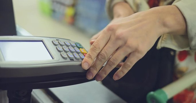 Woman pays for purchases. Girl inserts a bank card into the terminal and dials the pin code. Close-up.