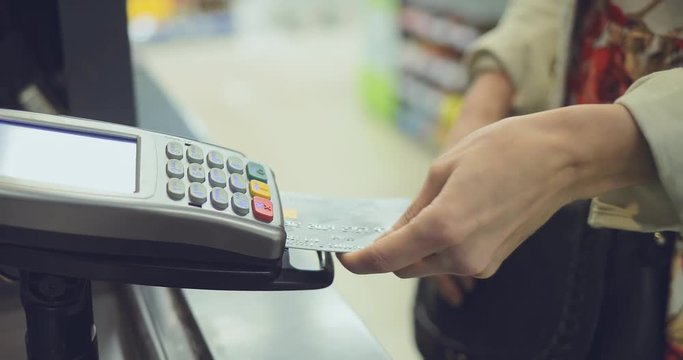 Girl inserts a card into the cash terminal and pays for purchases, dials the PIN code. Close-up.
