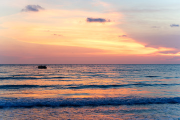 Colorful ocean beach sunset with deep orange blue sky and sun rays. Small waves coming on the beach. Travel and holiday on the beach concept.
