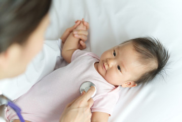 Obraz na płótnie Canvas Female doctor is listening heart pulse rate of Asian newborn baby smiling on the bed by using stethoscope in the room. Seen from top and behind of doctor. Baby health care concept.