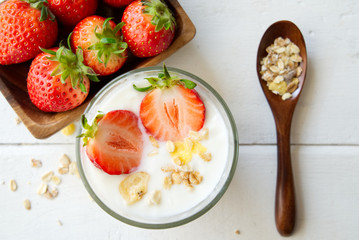 Healthy Greek yogurt with strawberry and muesli in the glass on a old wooden with table decorated with some of muesli and red strawberry and wooden spoon on the table. Seen in top close up view.