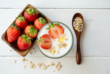 Healthy Greek yogurt with strawberry and muesli in the glass on a old wooden with table decorated with some of muesli and red strawberry and wooden spoon on the table. Seen in top view.
