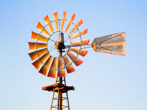 Windmill in Sunlight - An old metal windmill stands against a blue sky near sunset.