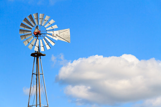 Windmill and Cloud - Antique metal windmill stands against a cloudy blue sky.