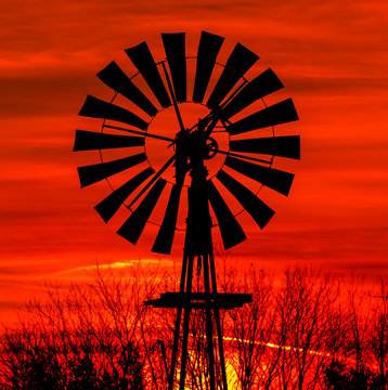 Windmill Sunrise Silhouette - Antique metal windmill silhouetted by a colorful orange sky.