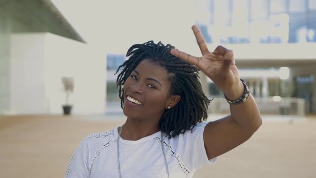 Smiling young woman with dreadlocks showing peace signs. Attractive African American girl looking at camera and gesturing. Gesture concept