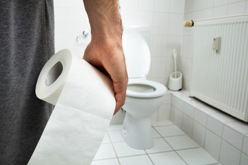Man Holding Tissue Paper Roll Standing In Front Of Toilet Bowl