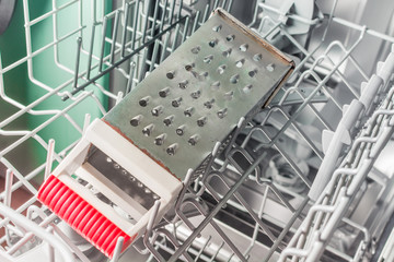 Iron grater with a red handle lies in the dishwasher
