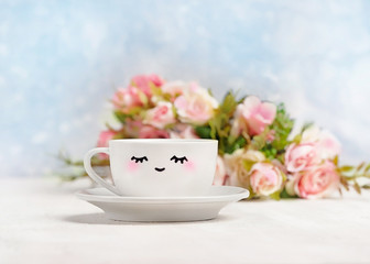 Obraz na płótnie Canvas white cup with cute smile. good morning, day start concept. Breakfast, smiling mug and flowers on white table. gentle romantic spring holiday image. soft focus