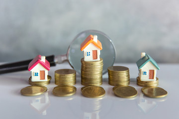 Miniature of house with magnifying glass and coin,  choice of location for the construction, of...