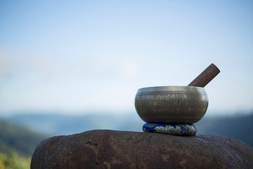 Tibetan singing bowl with sanskrit engraving pattern and sticks. on rock. morning natural background. copy space for text.(The Nepali word on the tibetan singing bowls means wish everything is fine.
