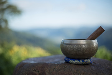 Tibetan singing bowl with sanskrit engraving pattern and sticks on the rock morning natural...