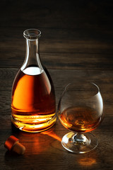view of glass of  whiskey and a bottle aside on color wooden  background. 