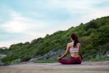 Fototapeta na wymiar Rearview of Healthy women wearing exercise clothes yoga. sitting in lotus pose meditation outdoors concentrating breathing asana yoga. .beautiful mountain landscape view sky on evening sunlight.