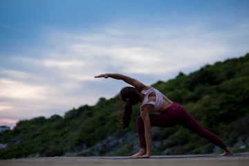 Rear view of healthy women practicing flexible yoga pose. stretching leg on mat on the rock. yoga...