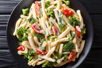 Delicious Italian pasta Casarecce with broccoli, garlic and tomatoes in a creamy sauce close-up on a plate. horizontal top view