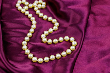 Pearl necklace on purple satin fabric background