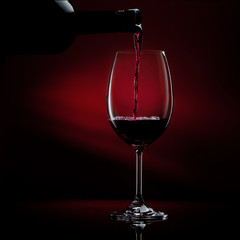 Naklejka na ściany i meble Red wine pouring in a glass from a bottle. Studio shot on black background.